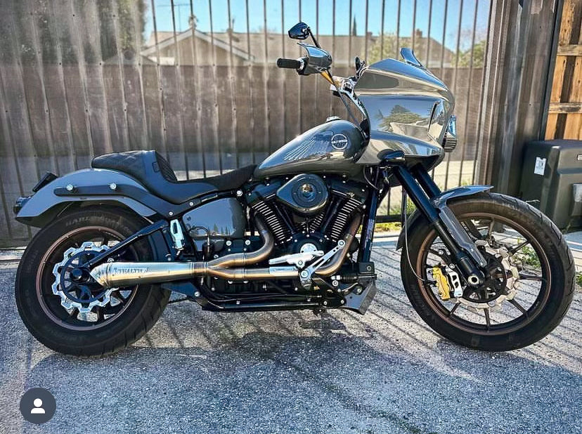 A black motorcycle with the focus on the exhaust system, which is silver in color. The motorcycle is parked against a plain wall backdrop., photo 27 of 36